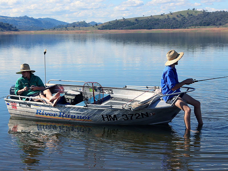 Two men sitting in tinny boat with fishing out of the boat with fishing rods.