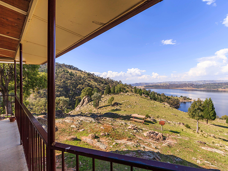 The view from a balcony at the top of a hill. There are rocky hills, trees and a large lake in the background.